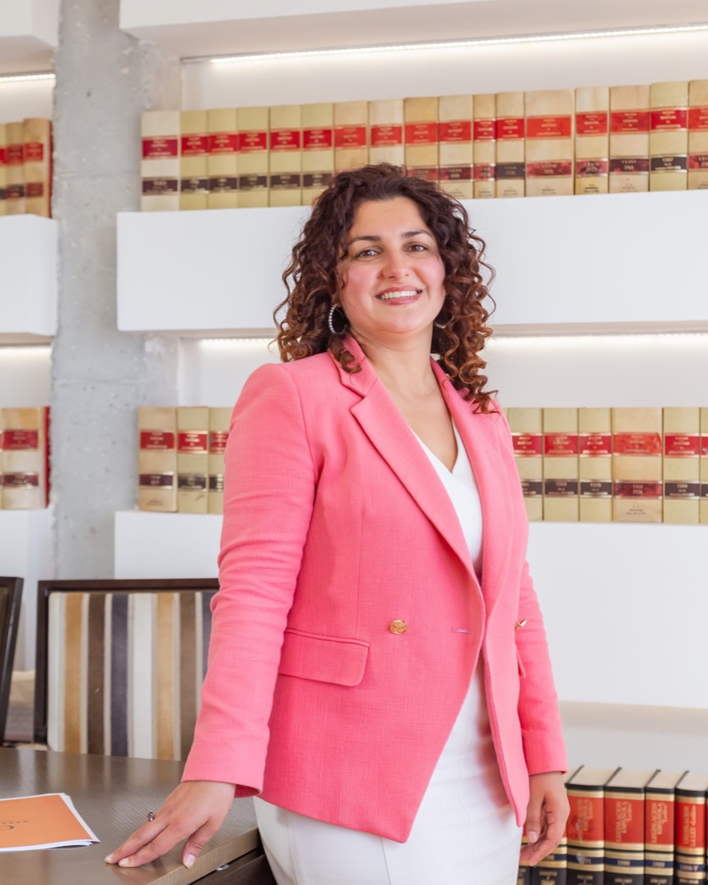 Portrait of Guzel Zamaltdinova at the firm’s offices, leaning on the meeting table in front of the shelves of law reports.