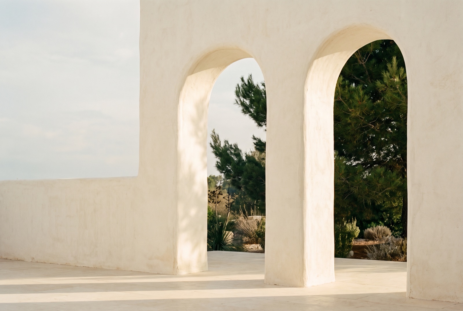Dos arcos gemelos abiertos al mismo jardín, con la luz de la mañana en el suelo de piedra