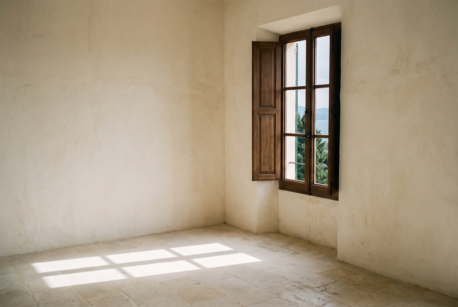 Ventana con contraventanas en una sala encalada, con la luz dibujando su escalera en el suelo